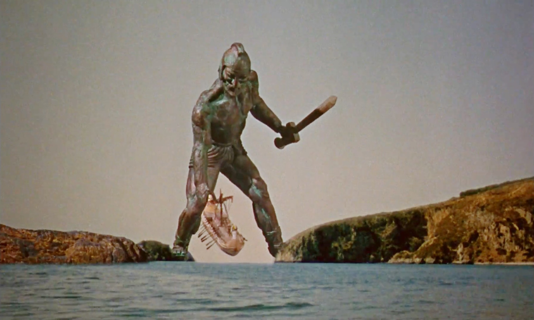 Talos from a classic film adaptation, towering over people on a beach.